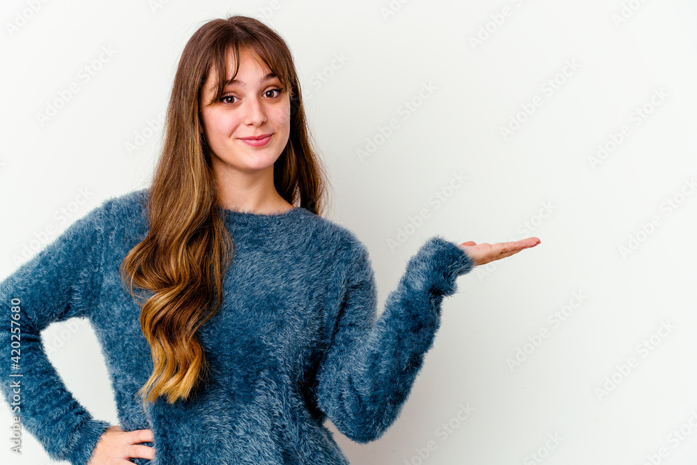 Young caucasian cute woman isolated on white background showing a copy space on a palm and holding another hand on waist. Young caucasian cute woman isolated on white background showing a copy space on a palm and holding another hand on waist.