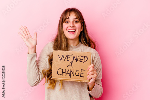 Young caucasian woman holding a We need a change placard isolated receiving a pleasant surprise, excited and raising hands.