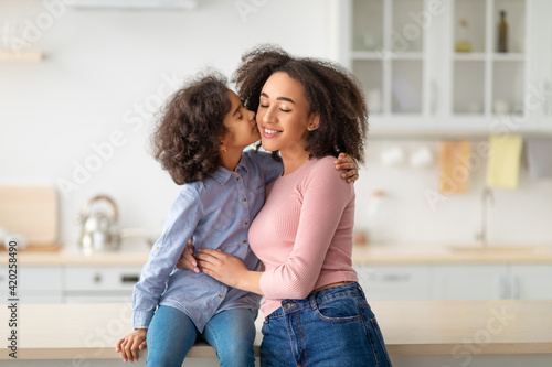 African American daughter hugging and kissing her smiling mum