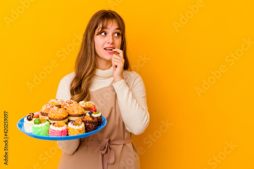 Young pastry chef woman isolated on yellow background relaxed thinking about something looking at a copy space.