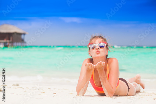 long haired woman in bikini and straw hat blowing a kiss on tropical beach