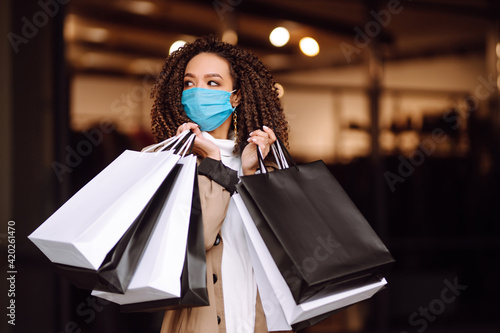 Portrait of beautiful african american woman in protective medical mask after shopping near the store. Shopping during the coronavirus Covid-19 pandemic. Sales And Discount, Retail, Purchase.