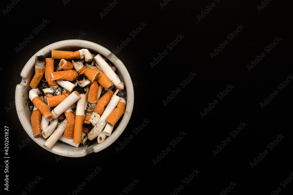 Ashtray with cigarette butts. Full of ashes. On a black background. Place for your text. Ashtray with cigarette butts. Full of ashes. On a black background. Place for your text.