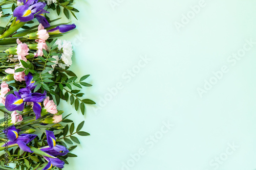 Mother's day or birthday background. Spring beautiful bouquet of blooming carnations and irises and spring greenery. Top view flat lay for greetings with space for text.
