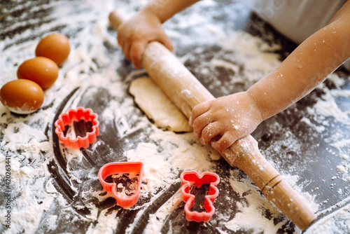 Φωτογραφία Little child  roll out the dough with a rolling pin on a wooden surface, close-up