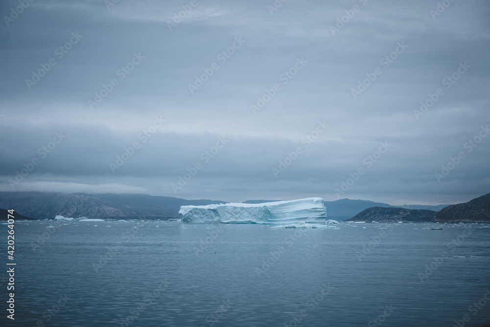 Obraz premium Arctic nature landscape with icebergs in Greenland icefjord with midnight sun sunset sunrise in the horizon. Early morning summer alpenglow during midnight season. Ilulissat, West Greenland.
