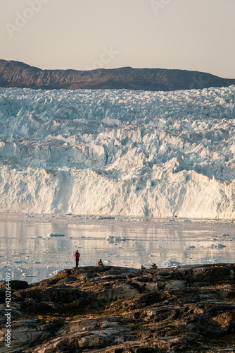 Unidentified People sitting standing in front of huge glacier wall of ice. Eqip Sermia Glacier Eqi glacier in Greenland called the calving glacier during midnight sun. Hikers during travel and photo