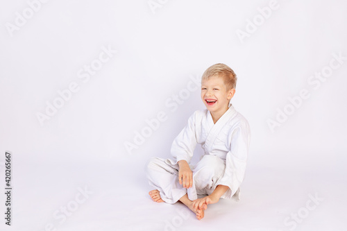 judo and sports concept, blond boy sitting in kimono on white background, place for text
