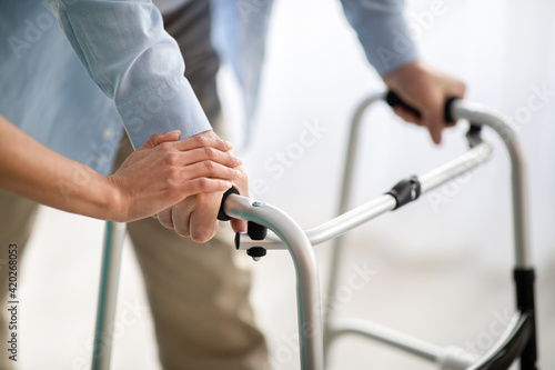Unrecognizable elderly man using walker, young doctor supporting and helping him at retirement home © Prostock-studio