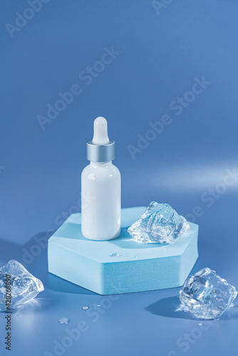 Skincare serum essence glass bottle on ice blue background. Concept summertime beauty product. Cooling summer facial care