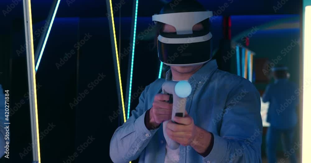 Young man in virtual reality glasses playing video games in cyber club. Gamer holding virtual gun to simulate shooting. Young man in virtual reality glasses playing video games in cyber club. Gamer holding virtual gun to simulate shooting.