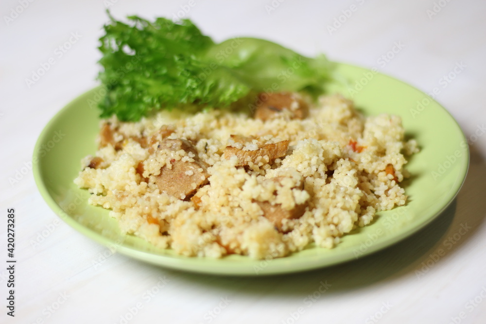 Cuscus with carrot, tomato, pork and salad leaf on green plate on white table Cuscus with carrot, tomato, pork and salad leaf on green plate on white table
