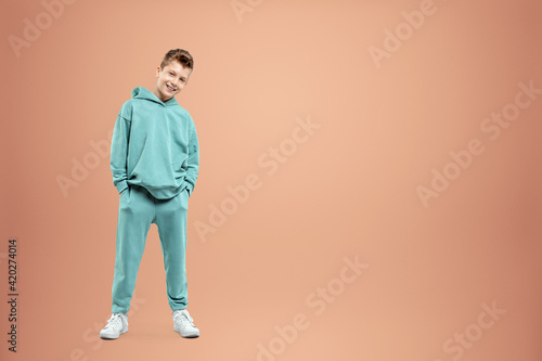 A boy in a turquoise suit posing and fooling around on a beige background, looking at the camera. Children's studio portrait. Childhood lifestyle concept.