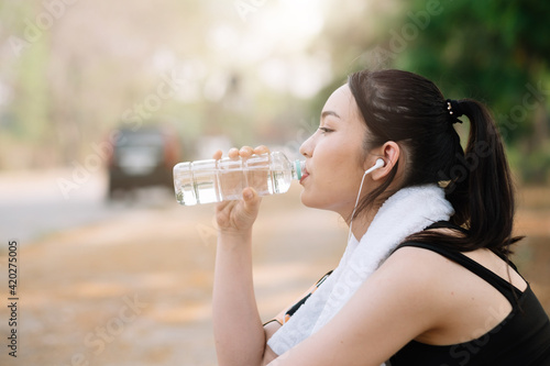 Young woman athlete takes a break, drinking water, out on a run on a hot day.