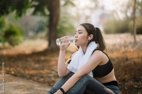 Young woman athlete takes a break, drinking water, out on a run on a hot day.