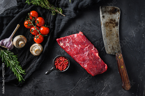 Raw, flap or flank, also known Bavette steak near butcher knife with pink pepper and rosemary. Black background. Top view photo
