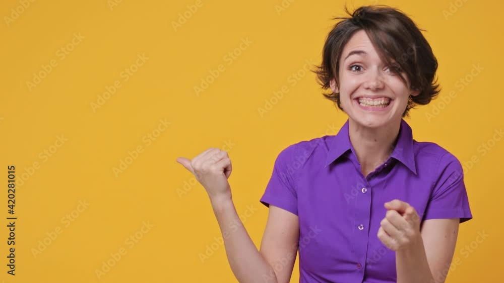 Smiling young promoter woman 20s in violet shirt recommend suggest select advert pointing fingers hands aside on workspace copyspace mockup promo commercial area isolated on yellow background studio Smiling young promoter woman 20s in violet shirt recommend suggest select advert pointing fingers hands aside on workspace copyspace mockup promo commercial area isolated on yellow background studio
