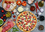pizza with salami, tomatoes, mushrooms and cheese. ingredients and spices on grey concrete background 