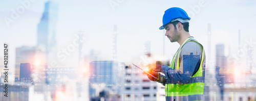 Fotografia, Obraz Panoramic double exposure of smart engineer maintenance in solar power plant checking installing photovoltaic solar modules with digital tablet with Oil and gas refinery industry plant background