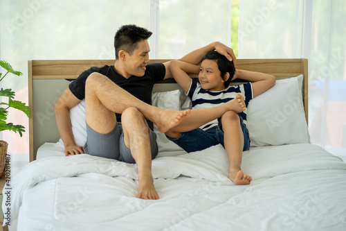 Asian young boy playing in white bed with father in new normal work from home
