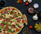 pizza with salami, tomatoes, mushrooms and cheese. ingredients and spices on black concrete background 