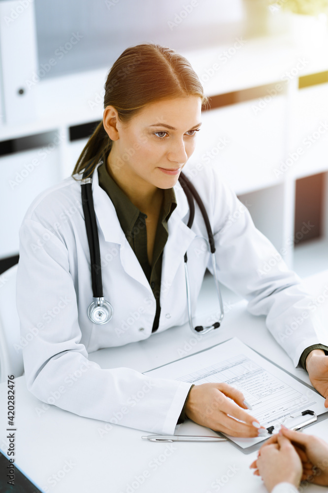 Woman-doctor and patient sitting and talking at sunny hospital office. Green color blouse suits to therapist. Medicine and healthcare concept Woman-doctor and patient sitting and talking at sunny hospital office. Green color blouse suits to therapist. Medicine and healthcare concept