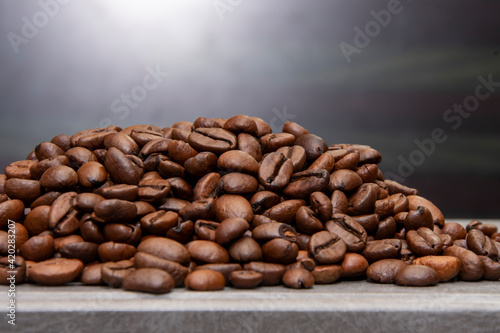 A pile of roasted coffee beans lying on the table, light glare, close-up, selective focus, space for text.