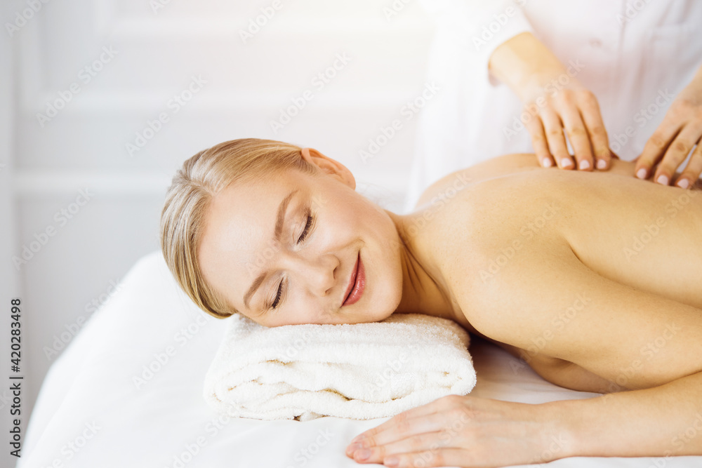 Beautiful caucasian woman enjoying back massage with closed eyes in sunny Spa salon Beautiful caucasian woman enjoying back massage with closed eyes in sunny Spa salon