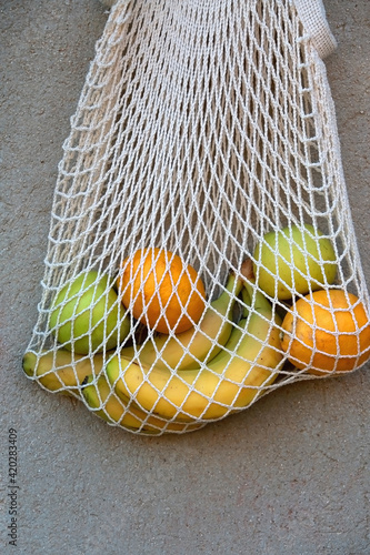Macrame bag filled with bananas, apples and lemons, hanging on the concrete wall.
