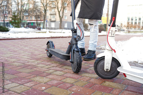 The electric scooter stands on the track in the park in the spring. There is snow all around