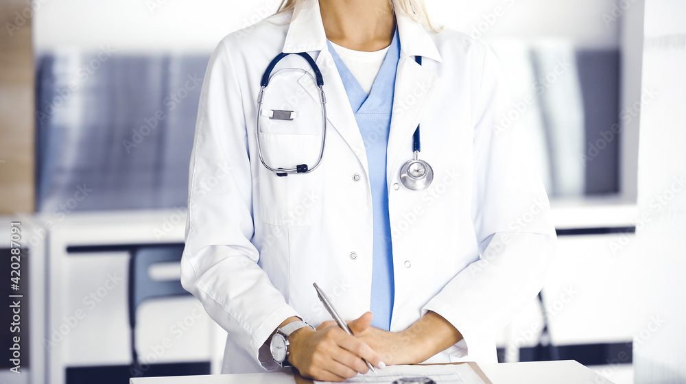 Unknown woman-doctor and patient in hospital. Blonde physician controls medication history records and exam results while using clipboard, close-up. Medicine concept Unknown woman-doctor and patient in hospital. Blonde physician controls medication history records and exam results while using clipboard, close-up. Medicine concept