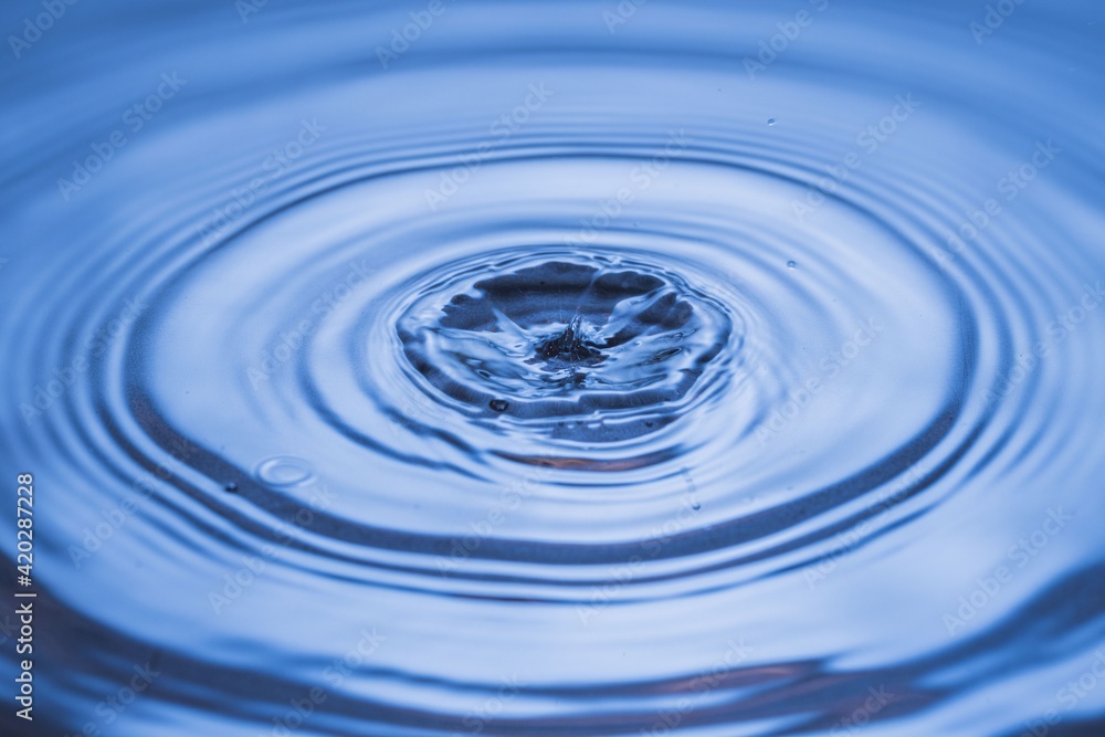 View of drops making circles on blue water surface isolated on background. View of drops making circles on blue water surface isolated on background.