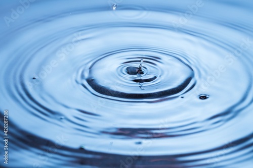 View of drops making circles on blue water surface isolated on background.