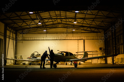 two men parking small jet in a hangar at night
