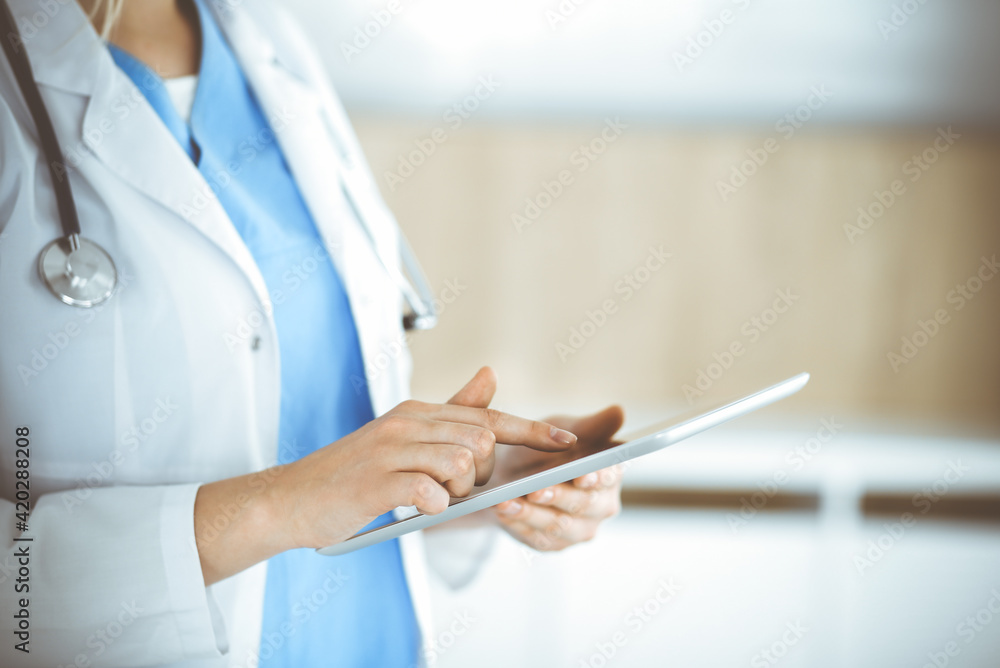 Unknown woman-doctor standing in clinic and using tablet pc, close-up. Data in medicine and healthcare Unknown woman-doctor standing in clinic and using tablet pc, close-up. Data in medicine and healthcare