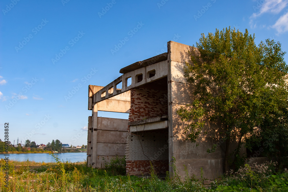 Abandoned panel building. Industrial building is abandoned. It is overgrown with grass and trees. Concept - abandoned building of a decayed factory. He is missing windows and part of walls
