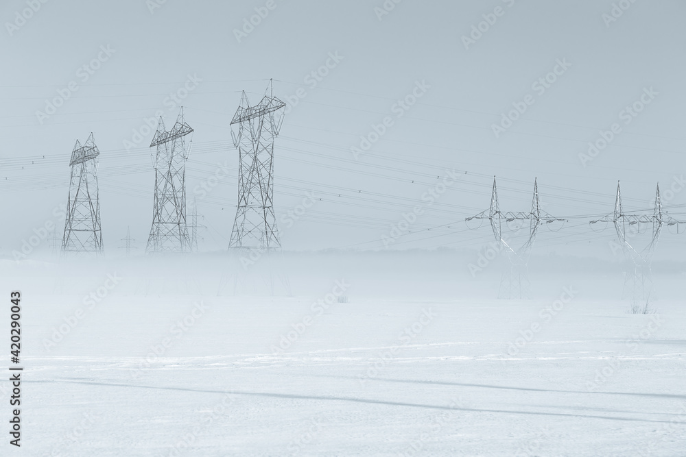 Fototapeta premium View of power line towers in fields with base shrouded in fog during a beautiful late winter early morning, Levis, Quebec, Canada