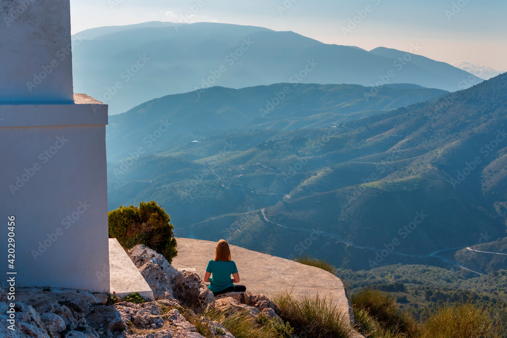 Φωτογραφία Woman practicing yoga next to a hermitage on top of a mountain, with spectacular views of other mountains at sunrise