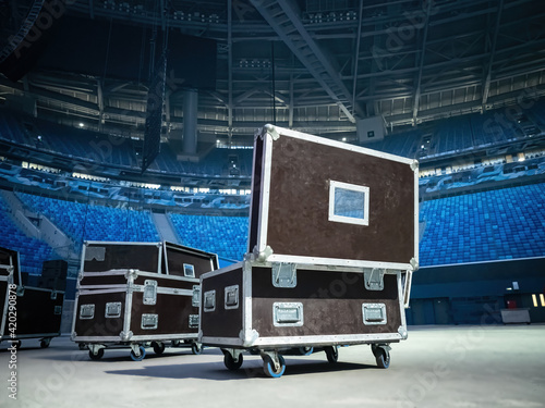 Concert equipment boxes. Stage equipment in transport boxes. Black wardrobe trunks on wheels. Equipment boxes on concert stage. Stadium stands in background. Concept - preparation for concert.