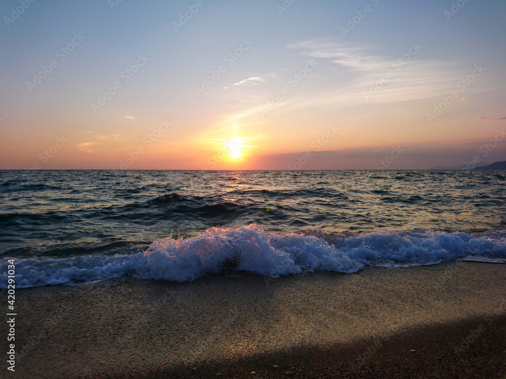 Orange sunset sun shining on sea shore with beautiful white waves. Summer sea idyllic travel, evening in Greece