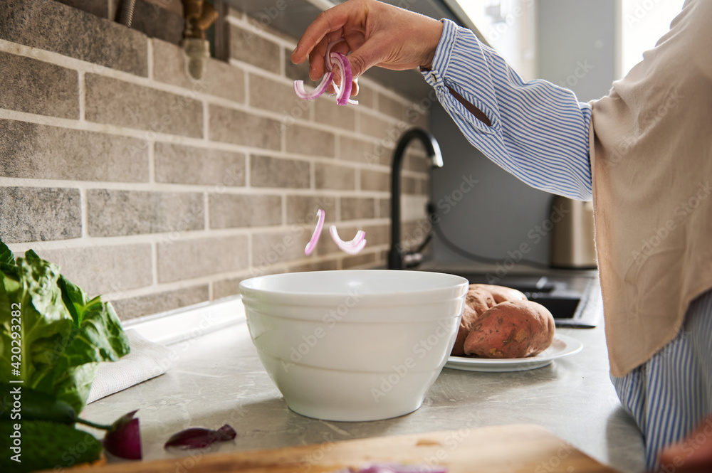 Close up of a white salad bowl and hand of a woman putting sliced onion on a bowl