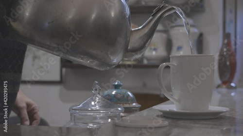 hand pours boiling water into a cup with herbal tea, then takes two biscuits and places them in a saucer