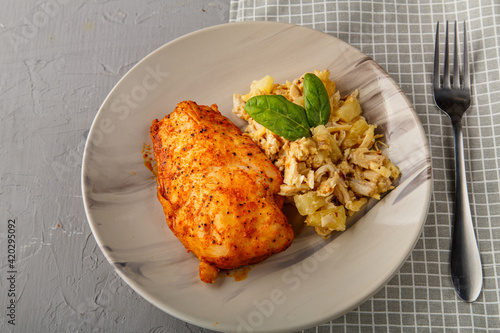 Baked chicken breast on a gray plate with pineapple salad on a table on a napkin on a concrete background near a fork.