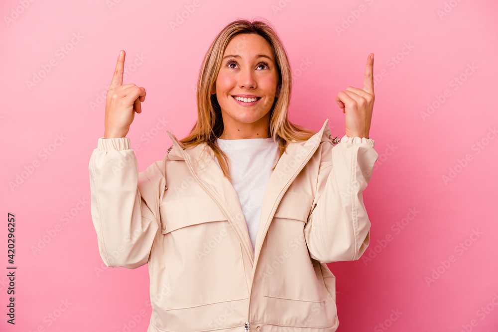 Young mixed race woman isolated on pink background indicates with both fore fingers up showing a blank space. Young mixed race woman isolated on pink background indicates with both fore fingers up showing a blank space.