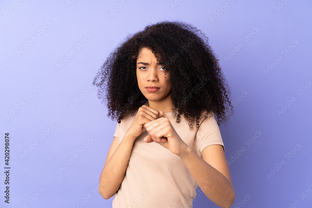 Young african american woman isolated on purple background with fighting gesture Young african american woman isolated on purple background with fighting gesture