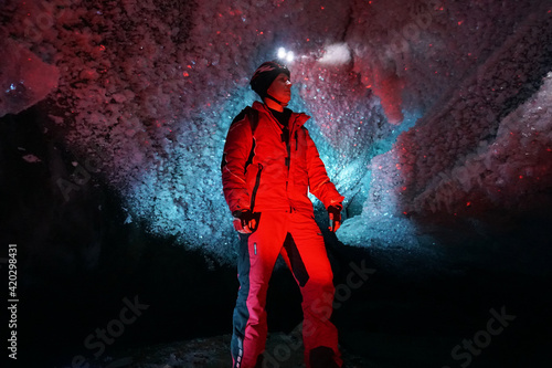 A guy in an ice cave with a lantern light. The caver descended into the ice cave. Snow stalactites and ice walls. In some places there are stones. Colored lantern beams. Bogdanovich Glacier, Almaty