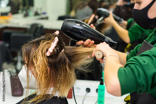 Hairdresser in a mask with at work, drying hair in a barbershop, client and stylist in masks.