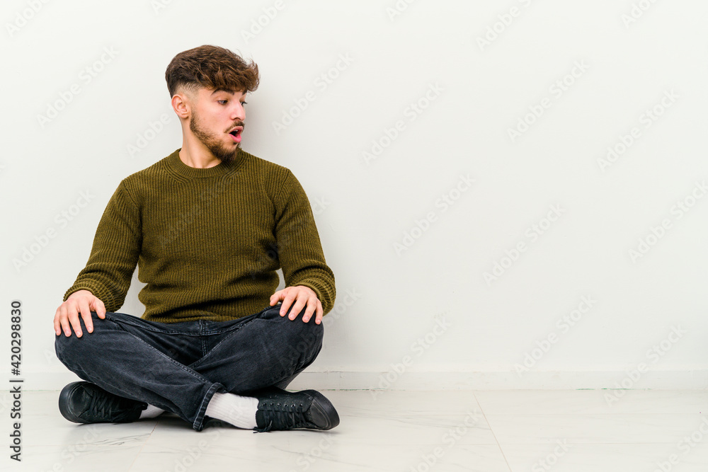 Young Moroccan man sitting on the floor isolated on white background being shocked because of something she has seen. Young Moroccan man sitting on the floor isolated on white background being shocked because of something she has seen.