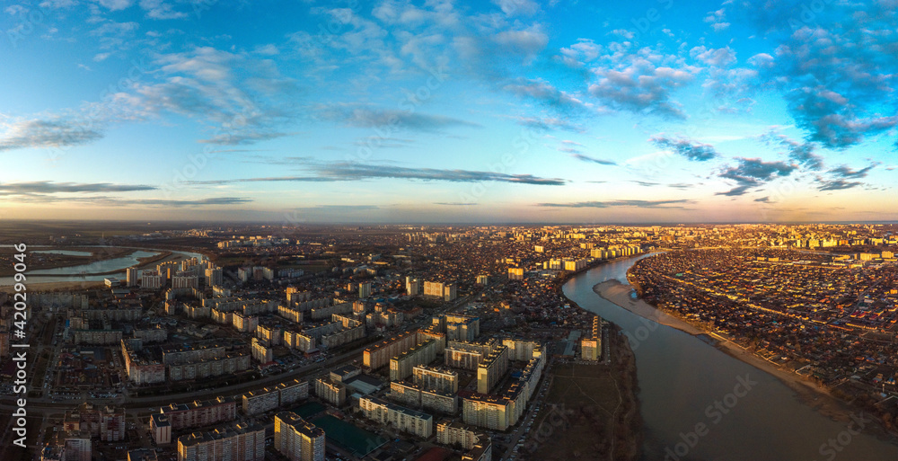 Obraz premium evening panoramic landscape of one- and multi-storey buildings and streets of the city of Krasnodar in the rays of the setting sun with blue sky and beautiful clouds