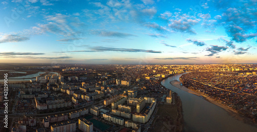 evening panoramic landscape of one- and multi-storey buildings and streets of the city of Krasnodar in the rays of the setting sun with blue sky and beautiful clouds